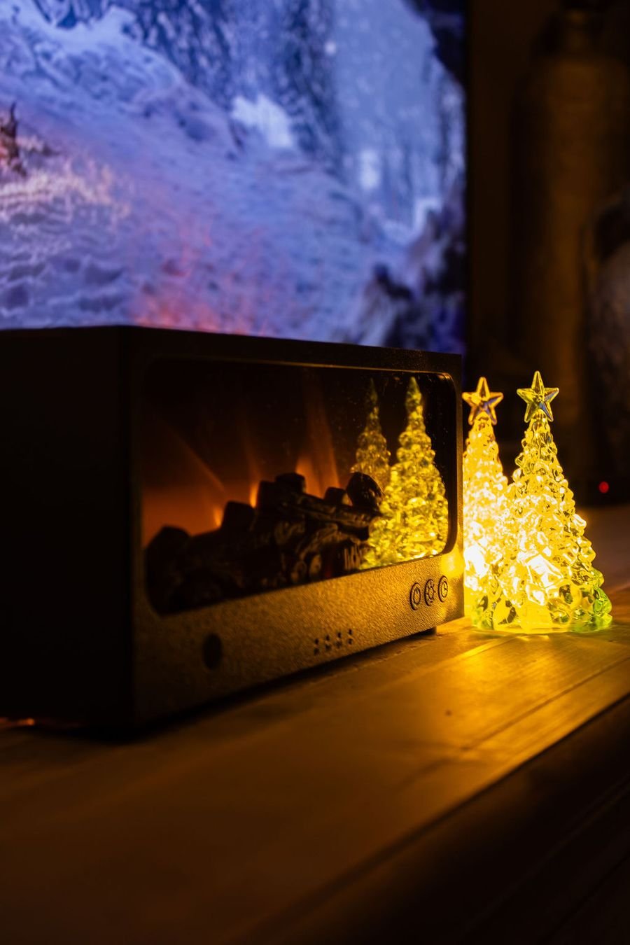 De zwarte Solafera Haard aan, met twee LED-boompjes ernaast op een houten kast